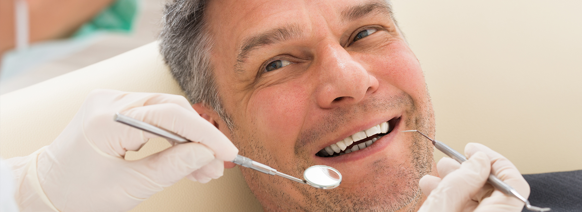 A man in a dental chair receiving dental treatment, with a dental hygienist attending to him.