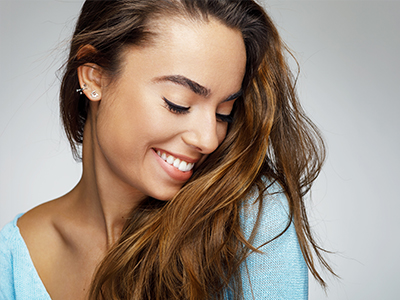 A woman with long brown hair, wearing a light blue top, smiles softly at the camera.