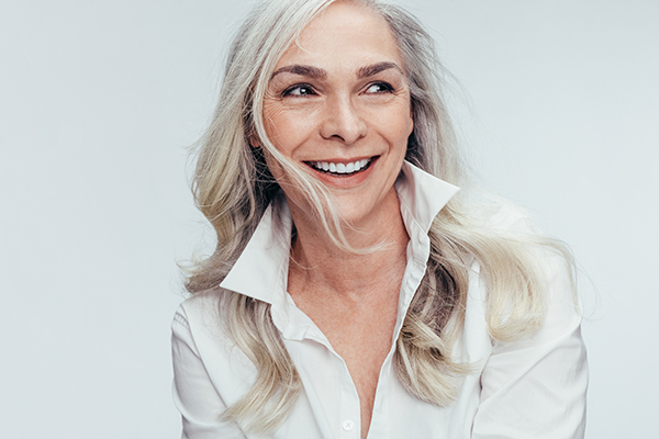 A woman with blonde hair and a white shirt smiles, looking directly at the camera.