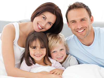 Happy family of four with two adults and two children, posing for a photo in bed.